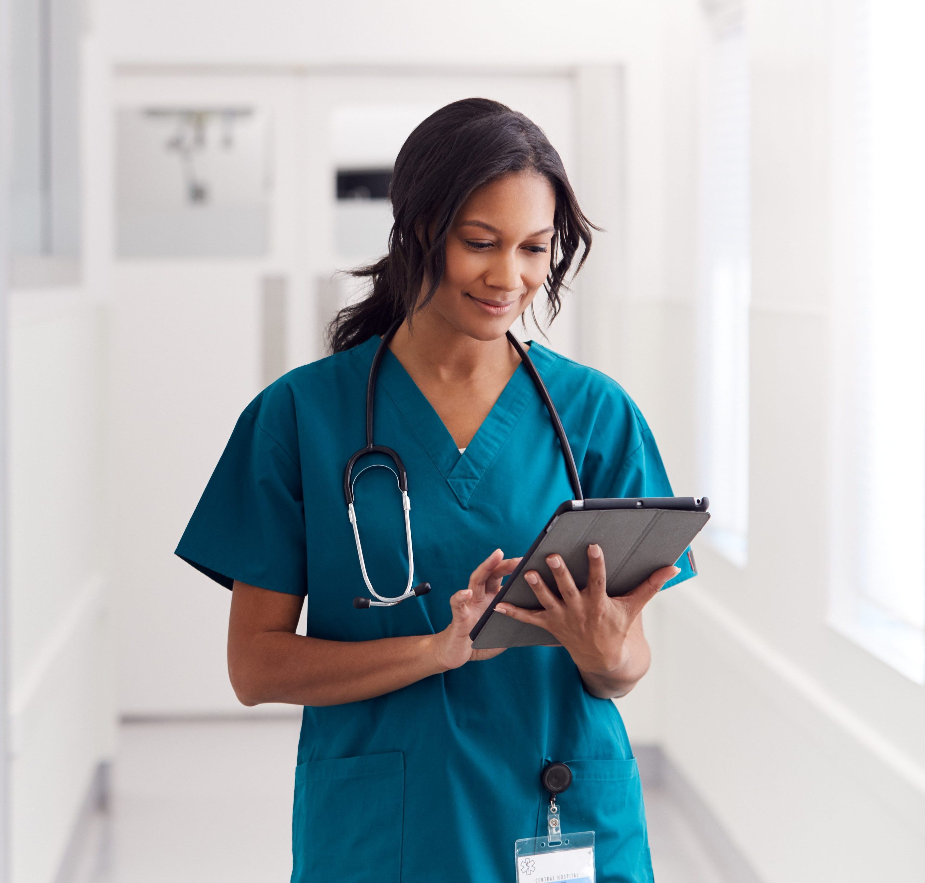 Female Doctor Wearing Scrubs In Hospital Corridor Using Digital Tablet